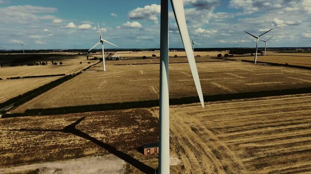 Aerial view of Burton Wold wind farm turbine 1 casting a long shadow over the golden agricultural fields of Burton Latimer, England, United Kingdom.