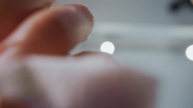 Close up of hand holding and unfolding white fabric in soft lighting. focus remains on delicate texture details as fingers manipulate material with blurred background emphasizing subject