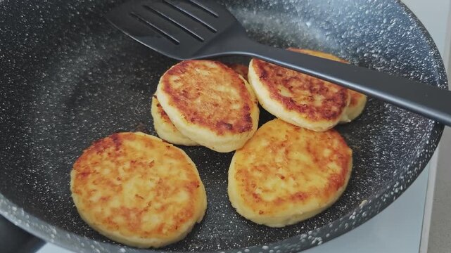 Closeup of syrniki, traditional eastern european cheese pancakes, frying in a non stick pan. Healthy homemade cooking for breakfast