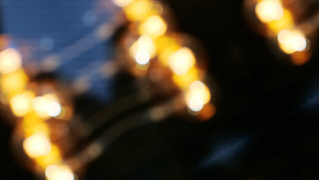 Defocused glowing warm yellow light bulbs bokeh background with dark atmosphere for festive holiday night celebration banner