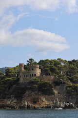 Fototapeta premium Historic castle and fortified walls of Vila Vella in Tossa de Mar, Costa Brava, Spain. Scenic Mediterranean coastline with medieval architecture, rocky cliffs and lush pine trees overlooking the sea.