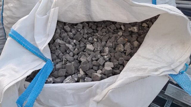 Granite crushed stone fraction 20-40 mm stacked inside a white soft big bag container close up. Construction building materials, wholesale industrial supply, real estate development.