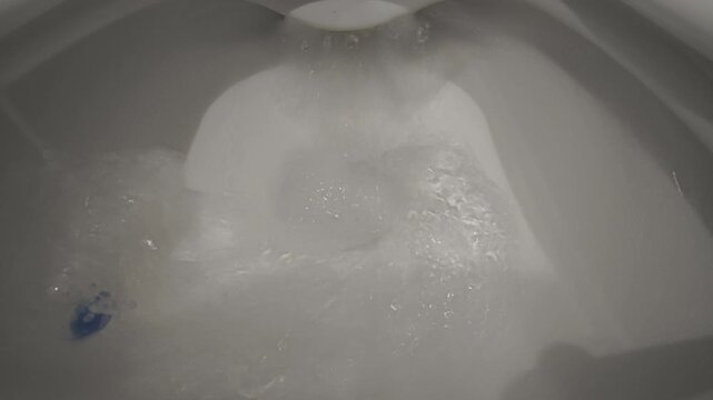 Water powerfully flushing down a clean white ceramic toilet bowl. A toilet freshener is attached to the rim ensuring hygiene and sanitation