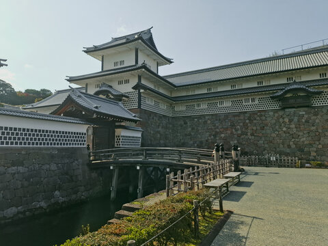View of the historic Kanazawa Castle with its traditional white walls, dark tiled roofs, and a wooden bridge over the moat in Kanazawa, Ishikawa, Japan.