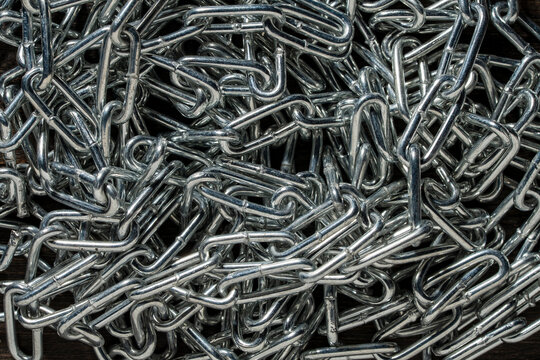 Tangled chrome steel chain top view texture background. Top-down view of tangled pile of shiny metallic chrome chains creating complex industrial pattern and texture with shadows, closeup