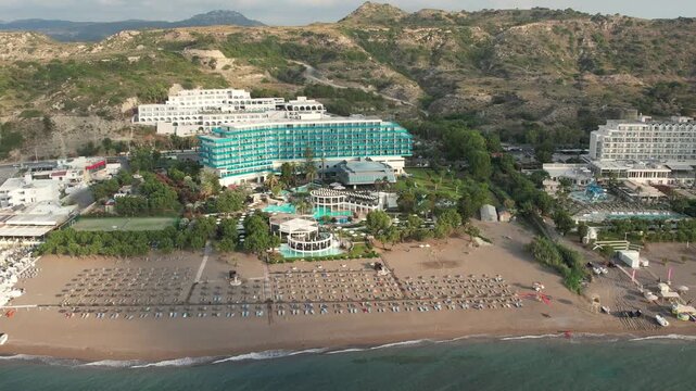 Beautiful aerial drone footage flying along Faliraki Beach on the island of Rhodes, Greece. Bird's-eye view of the long sandy coastline, crystal-clear Mediterranean Sea, beach resorts and hotels 