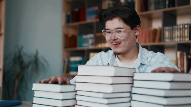 Happy student with glasses reading textbooks at wooden study desk focused on learning