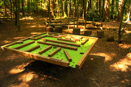 Wooden tilt labyrinth game in sunlit forest playground on outdoor trail.