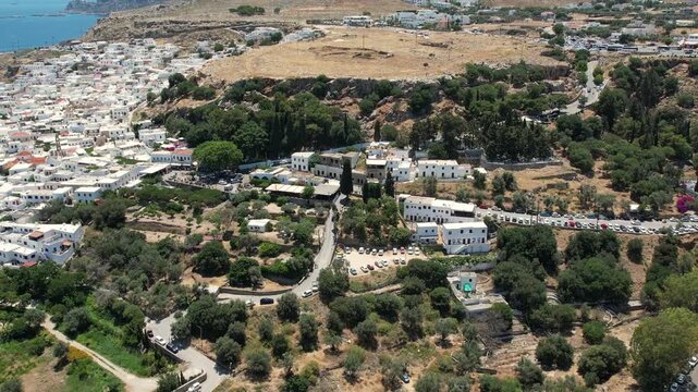 Stunning aerial drone footage flying over the ancient Acropolis of Lindos in Rhodes, Greece. The footage reveals the historic ruins perched above the picturesque whitewashed village of Lindos