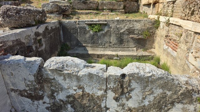 Athens, Greece - 4 July 2026. Ancient fountain basin in the Roman Forum, with plastered masonry, a recessed outlet, stone blocks, brickwork and grass.