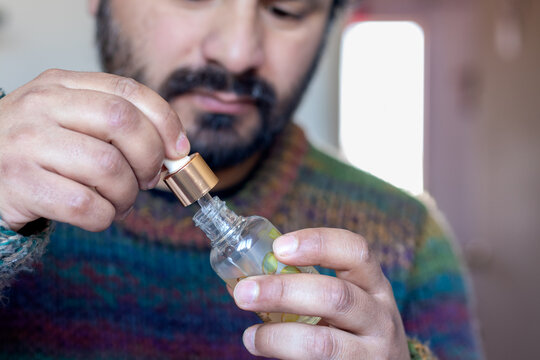 Bearded man opening a small glass dropper bottle