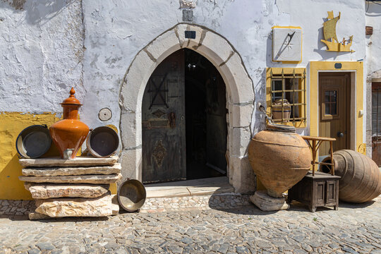 View of a historic arched stone doorway with traditional terracotta pottery, large clay amphorae, and a sundial on a white and yellow wall in Vila Vicosa, Distrito de Evora, Portugal.