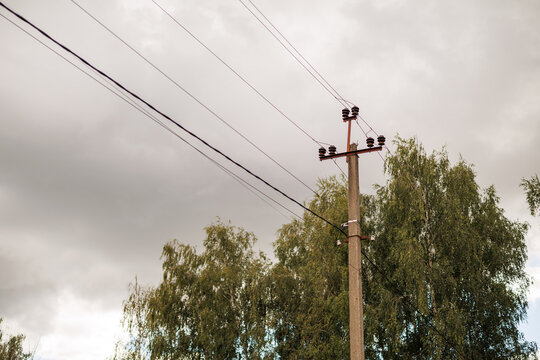 Concrete utility pole with power lines against a cloudy sky and green trees