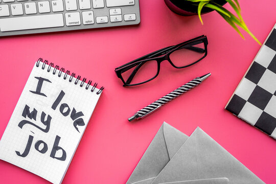 Find dream job. Handwritten motto I love my job in notebook on office desk on pink background top view