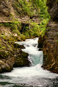 View of the rushing water and mossy rock formations of Vintgar Gorge with a wooden walkway along the cliffside in Bled, Radovljica, Slovenia.