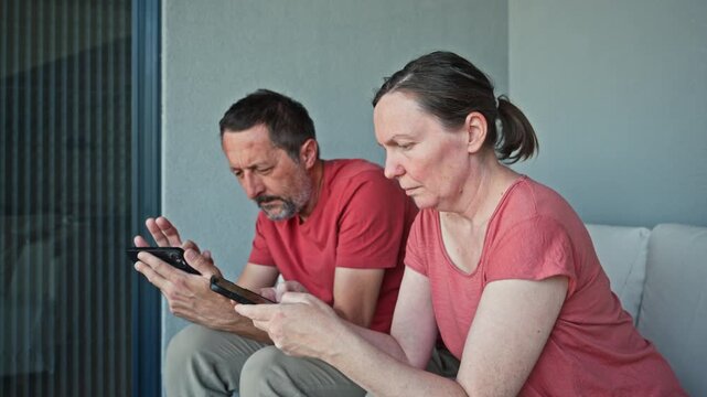 Mature adult man and woman sitting on a balcony sofa, each focused on their smartphone, emotionally distant and disconnected. 4K.
