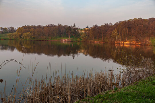 Beautiful scenic view of a forest lake with a historic palace mansion on a hill at sunset