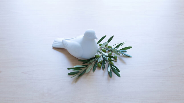 White ceramic dove figurine with green olive branch on wooden light surface.
