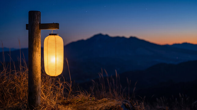 Traditional paper lantern glows against dark mountain sunset horizon.