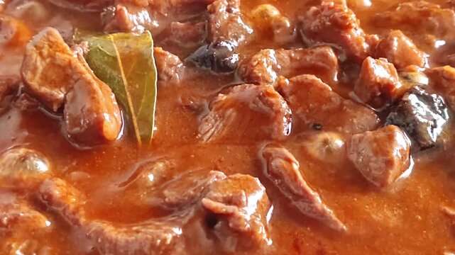 Slow cooking beef stew with rich gravy and bay leaf in a pan, close-up