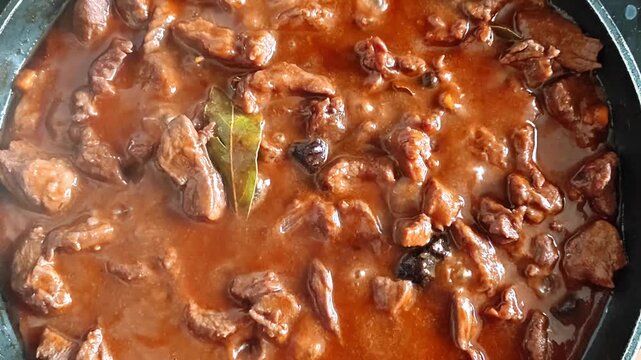Slow cooking beef stew with rich gravy and bay leaf in a pan, close-up