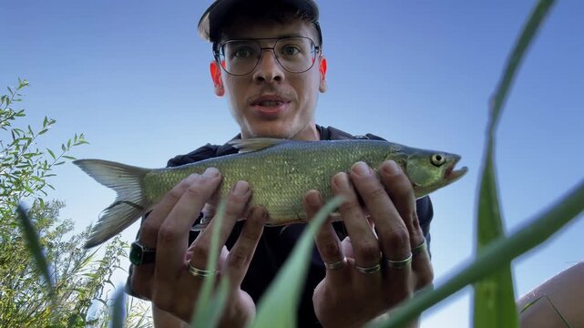 Portrait of a happy young fisherman smiling at camera holding a caught asp (Aspius aspius) outdoors. Catch and release hobby concept.