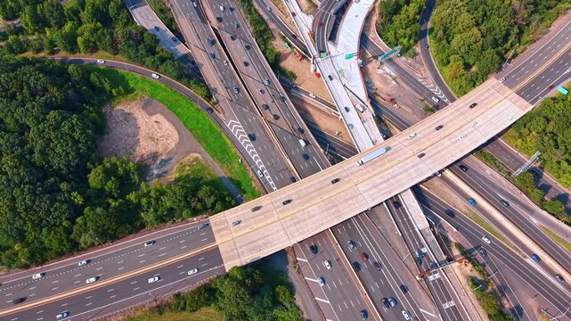 Complex road interchange connecting multiple asphalt lanes, New Jersey, USA. Overhead drone view of overlapping overpasses, moving cars and green landscape.