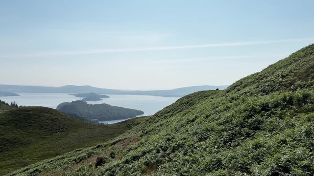 Panning view over green hillside covered with bracken ferns (Pteridium aquilinum) revealing large beautiful lake and mountains.