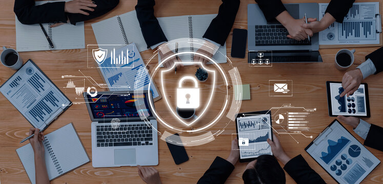 Professionals engage in a business meeting focused on digital security. Laptops and devices display charts and graphs, emphasizing collaboration and effective cybersecurity strategies. Trope