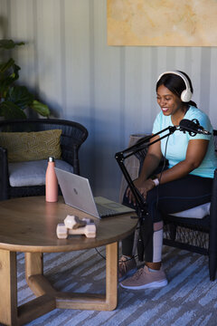 African woman recording in studio in sportswear with headset, near mic and laptop, copy space