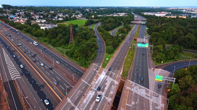 Elevated perspective of highway lane split and signs, New Jersey. View showing concrete road deck, moving vehicles and lush green trees.