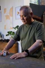 Fototapeta premium Senior Asian man wearing olive T-shirt and black wristwatch standing at home, gazing at toy car