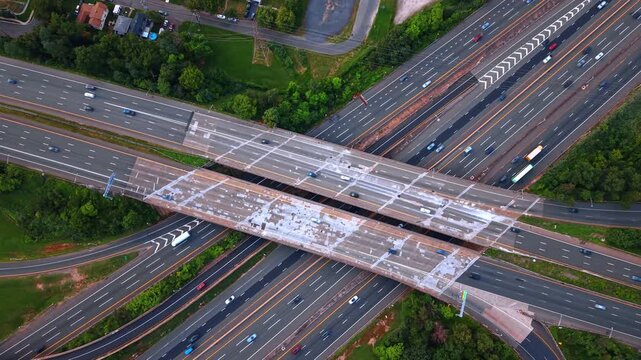 Large highway overpass crossing multi lane freeway, New Jersey. Direct overhead view of concrete bridges, moving cars and roadside foliage.