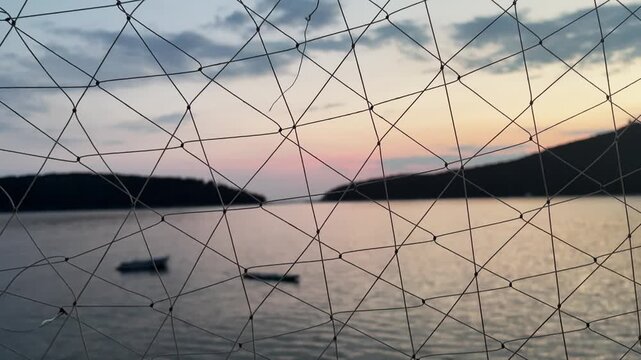 Blurred sea and island landscape at dusk viewed through a focused nautical fishing net, maritime concept.