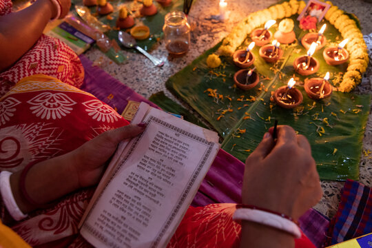 Dhaka, Bangladesh - 09 November 2021: View of a Hindu devotee reading prayers during the Rakher Upobash festival at Swamibag Loknath Temple, with oil lamps glowing on banana leaves.