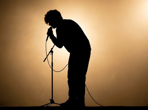 A silhouette of a person singing or speaking into a microphone against a warm, glowing background.