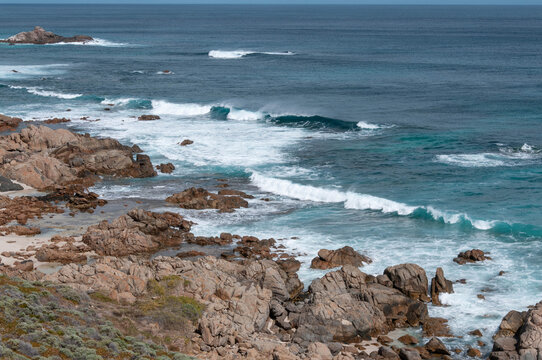 Turquoise ocean waves breaking around rugged rocks and a pale sandy cove in Western Australia.