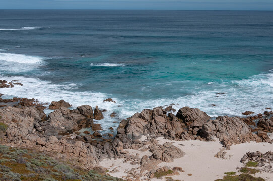 Weathered coastal formations frame clear blue water and a secluded beach in Western Australia.