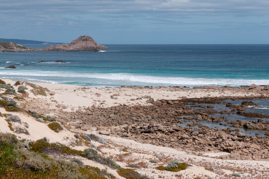 Western Australian beach with turquoise waves, pale dunes, rocky shoreline and a rugged offshore islet