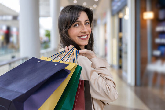 Waist up picture of a smiling dark-haired woman with shopping bags in hands