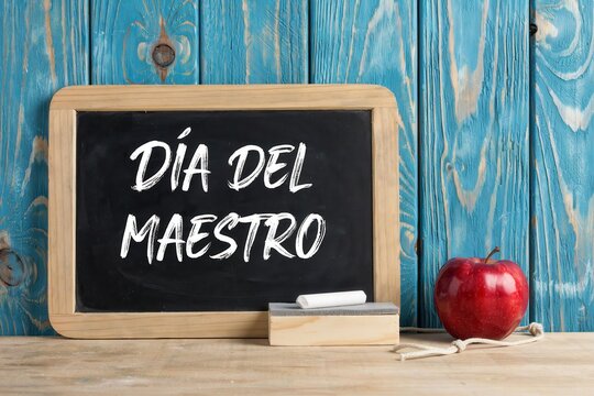 Chalkboard with the text dia del maestro and a red apple on a wooden table