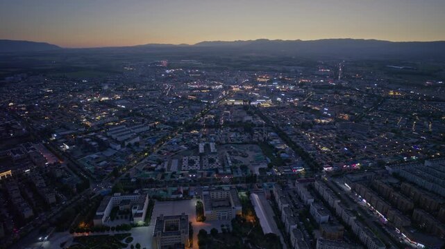 High-Angle Aerial Panoramic View of Tekes Bagua City Nightscape at Dusk, Ili Unique Bagua I-Ching Geometric Layout, City Lights, Radial Streets, Mountain Range and Horizon in Xinjiang