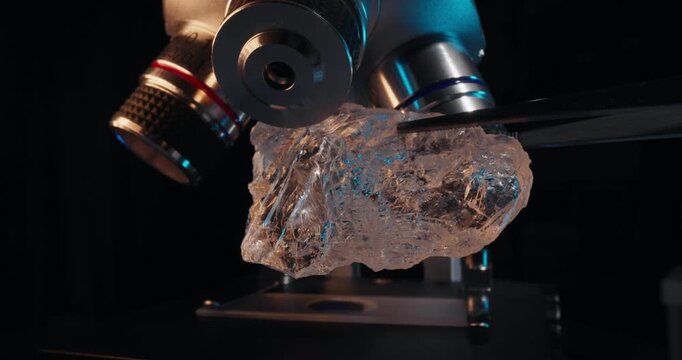 Rough nature diamond sample held by tweezers in front of microscope point for gemology research and laboratory.