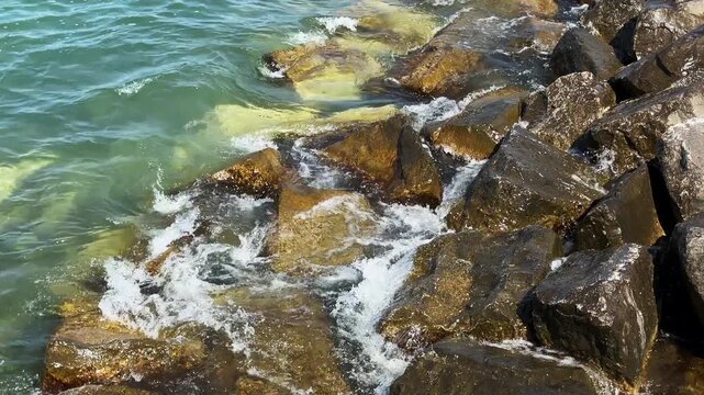 Close up of waves splashing on break wall rocks on a summer day.