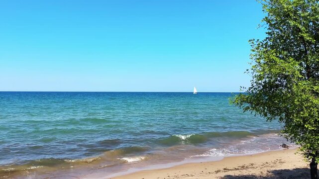 Tranquil summer scene of a sailboat sailing on Lake Michigan with gentle waves washing up on the sand