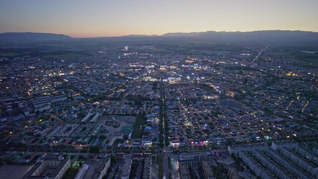 High-Angle Aerial Panoramic View of Tekes Bagua City Nightscape at Dusk, Ili Unique Bagua I-Ching Geometric Layout, City Lights, Radial Streets, Mountain Range and Horizon in Xinjiang