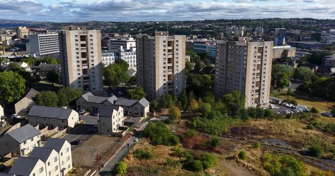 Aerial footage over Bradford in West Yorkshire showing three high rise residential tower blocks surrounded by modern housing mature trees open land and dense urban development across the city centre