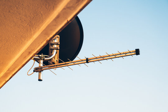 Television antenna and satellite dish installed on a house. Concept of media broadcasting, telecommunications, and connectivity.