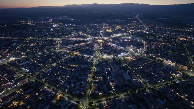 High-Angle Aerial Panoramic View of Tekes Bagua City Nightscape at Dusk, Ili Unique Bagua I-Ching Geometric Layout, City Lights, Radial Streets, Mountain Range and Horizon in Xinjiang