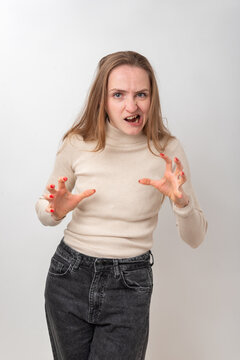 Young woman playfully expressing anger and aggression, adopting a monster like pose with a growling facial expression and clawed hands, standing against a clean white background
